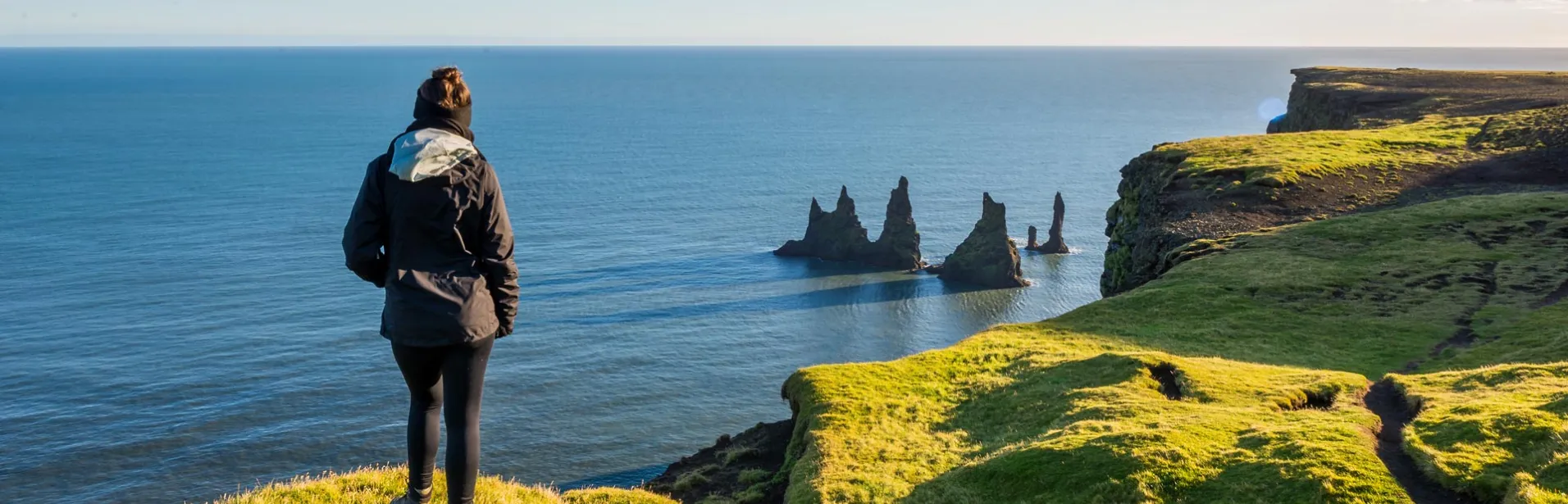 A person at Dyrhólaey overlooking Reynisdrangar and the Atlantic Ocean.