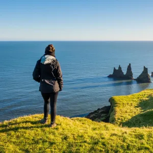 A person at Dyrhólaey overlooking Reynisdrangar and the Atlantic Ocean.