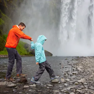 Father and son by waterfall Skogafoss in Iceland.